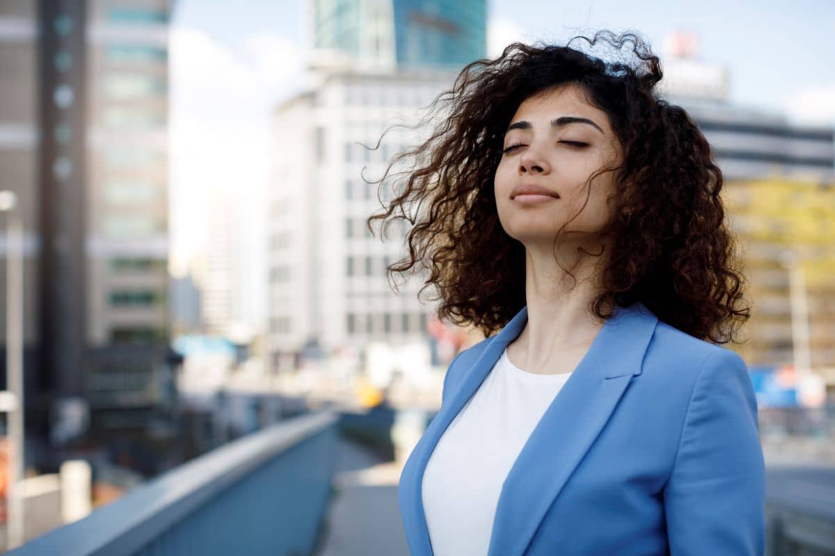 Nasal Congestion Blockage younger woman in an outdoor cityscape closing her eyes as the wind blows her hair forward